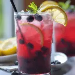 Refreshing blueberry tea lemonade in a glass with lemon slices and mint, perfect for summer gatherings.